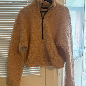 Beige teddytröja med half zip från SHEIN - Supermjuk och oversized beige teddytröja från SHEIN i storlek XS. Tröjan har en svart half zip-dragkedja, stor känguruficka och långärmad design. 