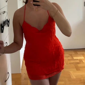 Röd/orange kort klänning med öppen rygg - Säljer en röd/orangd kort satin klänning med tunna axelband som korsas i ryggen och ger en snygg öppen rygg. Klänningen har en lätt draperad urringning och sitter figurnära. Passar nog även xxs. 