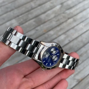Blå Marble Quartz klocka i metall - Snygg klocka från Marble med blå urtavla och tre mindre visartavlor. Armbandet är i blankt silverfärgat metall och boetten har detaljer med skruvar. Quartz-urverk och klassisk design som passar till många stilar. Lite trög när man ska sätta på