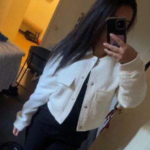 Vit croppad overshirt med knappar - Säljer en stilren vit croppad overshirt med silvriga knappar och två stora bröstfickor. Jackan har en strukturerad yta och är perfekt för dig som gillar en clean och trendig look. Passar snyggt till både jeans och kjol. Långärmad och med normal passform.