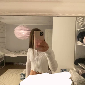 Vit croppad kofta från NA-KD - Säljer en vit ribbad kofta från NA-KD i croppad modell. Tröjan har lång ärm, dragkedja framtill och är tillverkad i mjukt stickat material. Perfekt för dig som gillar en clean och stilren look med lite edge.