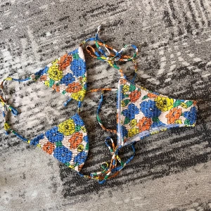 Blommig bikini med knytband - Superfin bikini med blommigt mönster i blått, gult, orange och grönt. Klassisk trekantsmodell med knyt i både topp och trosa. Materialet är stretchigt och smockat för en cool look. Perfekt för stranden eller poolen!