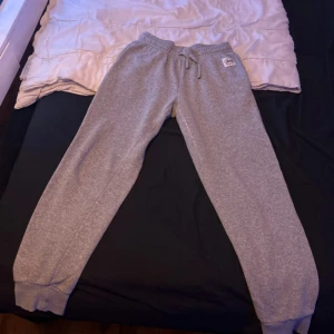 Grå mjukisbyxor från Andy by Frank Dandy - Grå mjukisbyxor från Andy by Frank Dandy i storlek S. Byxorna har resår i midjan med snörning och muddar vid bensluten. Tillverkade i en mjuk blandning av bomull och polyester för extra komfort. Perfekta för chill dagar eller träning.