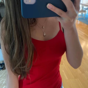 Röd linnetopp med smala axelband - Snygg röd linnetopp med smala axelband och figurnära passform. Perfekt till jeans eller kjol för en enkel och fräsch look. Toppens material känns mjukt och stretchigt, vilket gör den superbekväm att bära under varma dagar. Den är köpt i Mexiko så det står inget märke eller storlek på men skulle säga att den passar XS och S bra då den är stretchig.