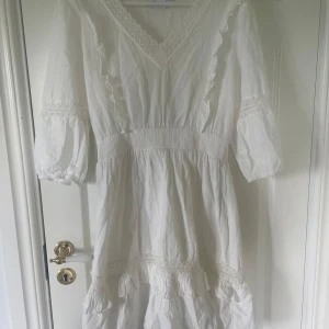 Vit kortklänning med spets från vila - Vit klänning från vila som endast blivit använd fåtal gånger men tyvärr är för stor. Den har v-ringning, volanger och spetsdetaljer.