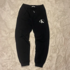 Svarta mjukisbyxor Calvin Klein Jeans - Svarta mjukisbyxor från Calvin Klein Jeans med vit CK-logga på benet. Byxorna har dragsko i midjan, ribbade muddar vid benslut och är tillverkade i mjukt material. Perfekta för chill dagar och har fickor på sidorna samt baktill.