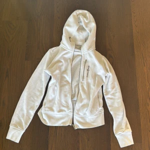 Vit hoodie från Sail Racing, M - Vit hoodie från Sail Racing med dragkedja framtill och broderad logga på bröstet. Knappast använd finns en gul liten fläck på insidan men inget som syns. Nypris är 1500kr men säljer för 350kr. Köpare står för frakten.
