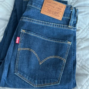 Levi's skinny jeans mörkblå denim - Mörkblå skinny jeans från Levi's med klassisk femficksdesign, snygga kontrastsömmar och ikonisk läderpatch bak. Hög midja och smal passform som sitter tajt hela vägen ner. Perfekta för dig som gillar en clean och tidlös denimlook.