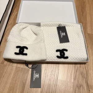Vit stickad halsduk från Chanel - Exklusiv vit stickad halsduk från Chanel med klassiskt svart CC-logo broderat i ena änden. Halsduken har en diskret strukturstickning som ger en lyxig känsla och är perfekt för kalla dagar. Kommer med originaltagg och box.