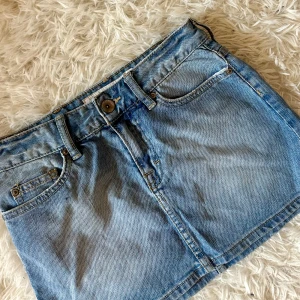 Ljusblå jeanskjol - Snygg ljusblå jeanskjol i klassisk modell med fem fickor, bälteshällor och knapp framtill. Kjolen är lågmidjad och kort.💕