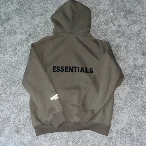 Essentials brun/grön zip-up hoodie - Säljer min Essentials brun/grön zip-up hoodie eftersom den inte passar mig längre. Det är en stilig och bekväm hoodie som passar för alla situationer. Den har bara använts ett fåtal gånger och därför är skicket utmärkt.