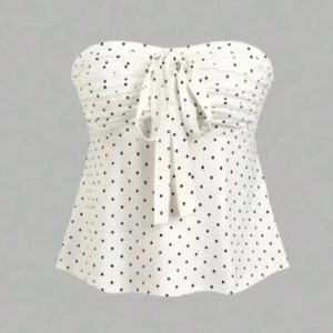 Vit prickig tubtopp med knyt - Supersöt vit tubtopp med svarta prickar och knyt framtill. Toppen är axelbandslös och har en lätt utsvängd passform, perfekt för varma dagar. Prickmönstret ger en lekfull vibe och knytet framtill gör den extra charmig.