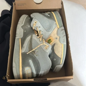 Nike Air Trainer 1 Cactus Corporation Travis Scott  - Unika Nike Air Trainer 1 Cactus Corporation sneakers i ljusgrått och beige med gröna detaljer. Skorna har coola mesh- och manchesterpaneler, snörning och dragkedja på hälen. Snygga kontrastsömmar och broderade loggor ger en riktigt streetig vibe.