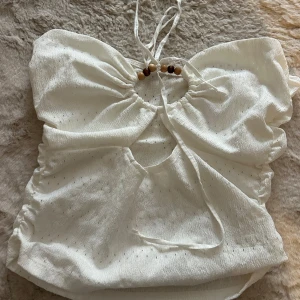 Vit linnetopp med knyt och pärldetalj - Superfin vitsommar topp med tunna axelband som knyts i nacken och träpärlor framtill. Toppen har en lätt rynkad struktur och en snygg cut-out detalj vid bysten. Storlek S🥹