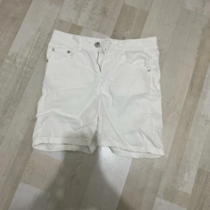Vita klassiska shorts med fickor - Snygga vita shorts med klassisk passform och fickor både fram och bak. De har bälteshällor och stängs med knapp och dragkedja. Perfekta för varma dagar och enkla att matcha med allt. Stilrena och fräscha shorts för en clean look.