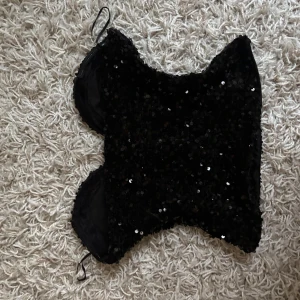 Svart paljett korsett-topp - Supersnygg svart korsett-topp och är täckt av glittrande paljetter. Toppen har en figurnära passform och en lätt hjärtformad urringning.