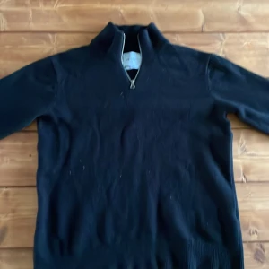 Svart merinoullströja från Vailent - Svart långärmad tröja från Vailent i mjuk merinoull. Tröjan har en hög krage med half zip-dragkedja. Står stl M i, men på grund av feltvättning uppskattas den till S. Inköpt på Carlings för 800 kr.