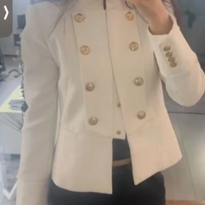 Vit kavaj med guldknappar från zara - Stilren vit kavaj från zara  med markerad axel och ståkrage. Dubbelknäppt framtill med snygga guldknappar med ankardetalj, samt fyra matchande knappar vid ärmslut. Figursydd passform och helfodrad, perfekt för en chic look.