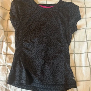 Leopardmönstrad träningst-shirt - Svart kortärmad träningst-shirt från SOC med diskret leopardmönster. Gjord i ett lätt och stretchigt syntetmaterial som andas, perfekt för sport eller gym. Rund halsringning med rosa detalj på insidan av kragen. Sitter snyggt och följsamt på kroppen. Passar även mig som vanligtvis har 146/152 eller xxs