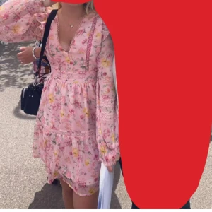 Rosa blommig kortklänning med volang - Supersöt rosa kortklänning med blommigt mönster i gult och grönt. Klänningen har v-ringning, långa ärmar med volangdetaljer och spets, samt markerad midja. Perfekt för sommarens alla tillfällen och ger en romantisk vibe. I storlek 36 men passar 34/32 med aldrig använt