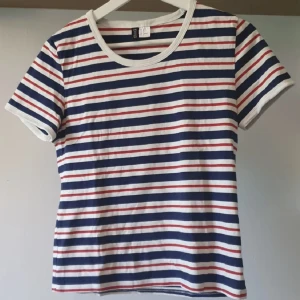 Randig t-shirt från H&M Divided - Säljer en klassisk randig t-shirt från H&M Divided i storlek M. T-shirten har vita, blåa och röda horisontella ränder, rund halsringning och korta ärmar. Mjuk o bekväm!