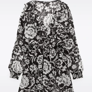 Blommig svartvit klänning från Zara - Supersnygg svartvit klänning från Zara med stora blommor, v-ringning och volangdetaljer. Långa ärmar med resår vid handlederna och markerad midja. Perfekt för dig som vill sticka ut med ett coolt mönster.