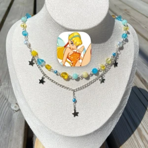 Färgglatt pärlhalsband med stjärnhängen - Unikt halsband med pärlor i blått, gult och vitt, mixat med silverfärgade kedjor och små stjärnhängen. Halsbandet har dubbla lager och coola detaljer som ger en lekfull och trendig vibe. Perfekt för dig som vill sticka ut med färg och personlighet. Halsbandet är inspirerat av karaktären Stella från tv-serien Winxclub och är det sista i min serie av Winxinspirerade halsband. 