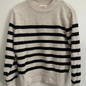 Stickad tröja från H&M - Snygg stickad tröja i beige med svarta horisontella ränder. Tröjan har rund halsringning, ribbade muddar och lång ärm. Perfekt för lager-på-lager och passar till både jeans och kjol.