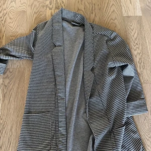 Rutig kavaj från FB Sister, storlek M - Snygg rutig kavaj från FB Sister i svart och vitt. Klassisk modell med krage och långa ärmar, perfekt för att lyfta vilken outfit som helst. Mjukt material som känns skönt mot huden och två stora fickor framtill.