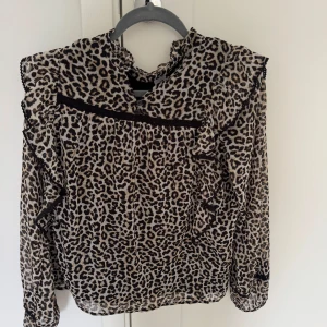 Leopardmönstrad blus från Lindex☺️ - Snygg blus från Lindex i leopardmönster med volangdetaljer och svarta spetsband. Lätt och luftig med knappar i halsen och långa ärmar. Perfekt för dig som vill sticka ut med en trendig look.