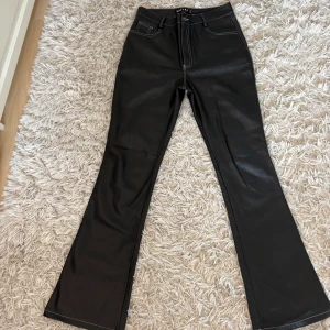 Skinbyxor bootcut  - Snygga svarta byxor från Motel i skinnimitation med vita kontrastsömmar. Modellen är bootcut med hög midja och klassiska fickor både fram och bak. Perfekta för dig som vill ha en edgy vibe och sticka ut lite extra. Skriv frågor och skicka gärna prisförslag!💕
