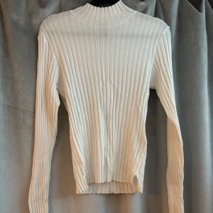 Vit ribbad polotröja med lång ärm - Snygg vit ribbad polotröja med lång ärm och hög hals. Tröjan har en tight passform och är tillverkad i ett stretchigt material som sitter skönt på kroppen. Använt några gånger.