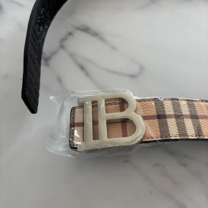 Burberry bälte med  - Snyggt Burberry bälte som man kan använda på två sidor den svarta och beiga. Perfekt accessoar för att lyfta vilken outfit som helst.