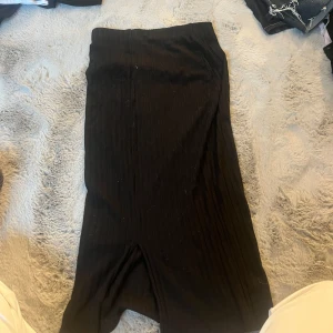 Svart ribbad långkjol från H&M XS - Svart ribbad långkjol från H&M i storlek XS. Kjolen har en tight passform och är tillverkad i ett stretchigt material som sitter snyggt. Perfekt för dig som gillar en enkel men stilren look.