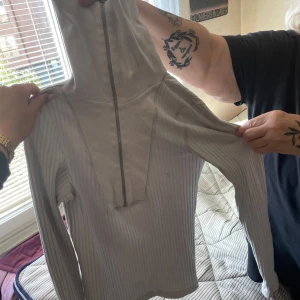 Ljusgrå ribbad tröja från Nelly - Supersnygg ljusgrå ribbad tröja från Nelly med lång ärm och half zip-dragkedja framtill. Tröjan har en tight passform och är tillverkad i mjuk bomullsmix. Perfekt till lager-på-lager och funkar året runt.