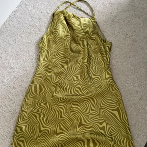 Grön mönstrad kortklänning med halterneck från Zara - Säljer en cool grön kortklänning med psykedeliskt mönster och halterneck-band från Zara. Klänningen har en figurnära passform och är perfekt för dig som vill sticka ut. Materialet känns slätt och svalt mot huden.