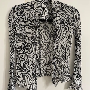 Zebramönstrad skjorta från Zara - Säljer en tunn och transparent skjorta med svartvitt zebramönster från Zara. Skjortan har långa ärmar och en lätt, flowy känsla som ger en cool och edgy vibe. Perfekt för dig som vill sticka ut med ett djurmönster i garderoben.