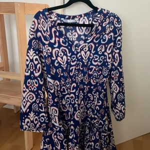 Mönstrad blå klänning från Zara - Snygg långärmad klänning från Zara med ett unikt blått och vitt mönster. Klänningen har v-ringning och en lös passform som ger en avslappnad vibe. Perfekt för dig som gillar färg och mönster! Aldrig använd 