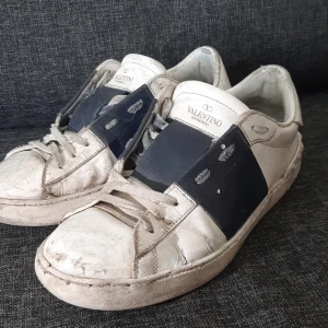 Valentino Garavani vita sneakers - Snygga vita sneakers från Valentino Garavani med bred mörkblå rem över vristen och klassisk snörning. De är använda och behöver bara en tvätt!