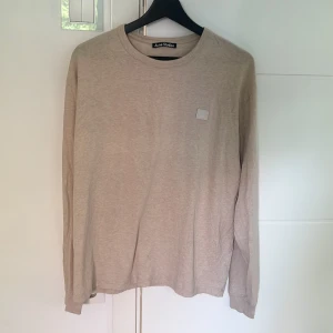 Beige långärmad tröja Acne Studios - Snygg beige långärmad tröja från Acne Studios med klassisk rund hals och diskret logopatch på bröstet. Tillverkad i mjuk bomull som känns skön mot huden. Perfekt för en clean och stilren look. NYPRIS 1300kr