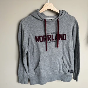 Grå hoodie från SQRTN Company XXS - Grå hoodie från SQRTN Company med vinröda snören och broderad text 'NORRLAND' på bröstet. Klassisk känguruficka framtill och huva. 