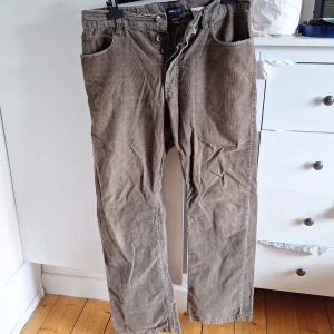 Bruna manchesterbyxor från H&M L.O.G.G. - Säljer ett par bruna manchesterbyxor från H&M L.O.G.G. med klassisk rak passform och knappgylf. Byxorna har fem fickor och är tillverkade i mjuk manchester, perfekta för dig som gillar en avslappnad men ändå stilren look.