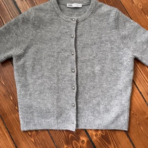 Grå kofta från Zara med knappar - Mysig grå kofta från Zara i storlek L men passar S/M. Koftan har rund halsringning, långa ärmar och silverfärgade knappar framtill. Tillverkad i ett mjukt, stickat material som passar perfekt för kyligare dagar.