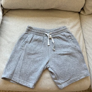 Grå mjukisshorts från H&M Divided XS - Gråa mjukisshorts med elastisk midja och vit snörning. Två fickor fram och en bakficka.