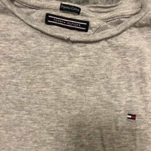Grå långärmad tröja Tommy Hilfiger - Snygg grå långärmad tröja från Tommy Hilfiger i mjuk ekologisk bomull. Klassisk passform med rund hals och diskret logga broderad på bröstet. Perfekt basic-plagg att ha i garderoben.