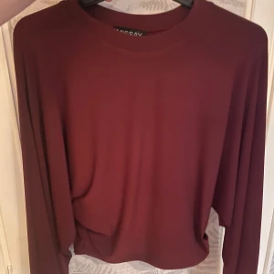 Vinröd långärmad tröja från Tussay - Vinröd långärmad tröja från Tussay med rund halsringning. Tröjan har en enkel och stilren design med loose passform och är tajtare i midjan, perfekt för dig som gillar en avslappnad look. Materialet känns mjukt och följsamt mot huden. 