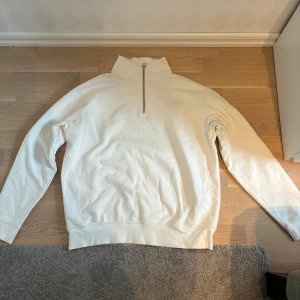 Vit half zip tröja från Zara - Vit långärmad tröja från Zara med hög krage och half zip-dragkedja. Tröjan är i mjuk bomull och har en clean, enkel look som passar perfekt till jeans eller joggers. Oversized känsla och riktigt skön att bära under lite kyliga dagar.