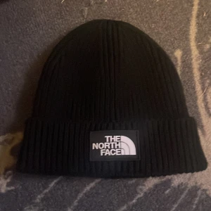 Svart  mössa från The North Face, helt ny utan prislapp  - Svart ribbstickad mössa från The North Face med uppvikt kant och tydlig logotyp framtill. Klassisk och stilren design som passar perfekt till kyliga dagar.