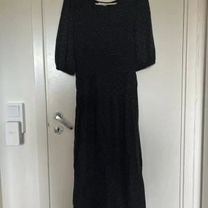 Svart klänning med prickar från Cubus - Säljer en elegant svart klänning med små vita prickar från märket C. Klänningen har korta ärmar och en smickrande passform som passar perfekt för olika tillfällen. Den är tillverkad i ett mjukt och bekvämt material. Ger lite 90 tals vibes! Perfekt om man ska klä ut sig till 90 tals tema!