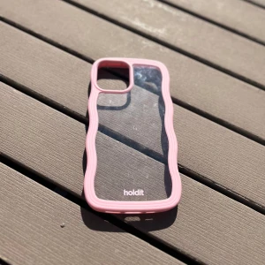 Rosa mobilskal från Holdit - Säljer ett genomskinligt mobilskal från Holdit med vågiga rosa kanter. Skalets design är modern och lekfull, perfekt för dig som vill ha ett snyggt och skyddande skal till mobilen. Passar till iPhone-modeller med dubbla kameror. Till iPhone 12